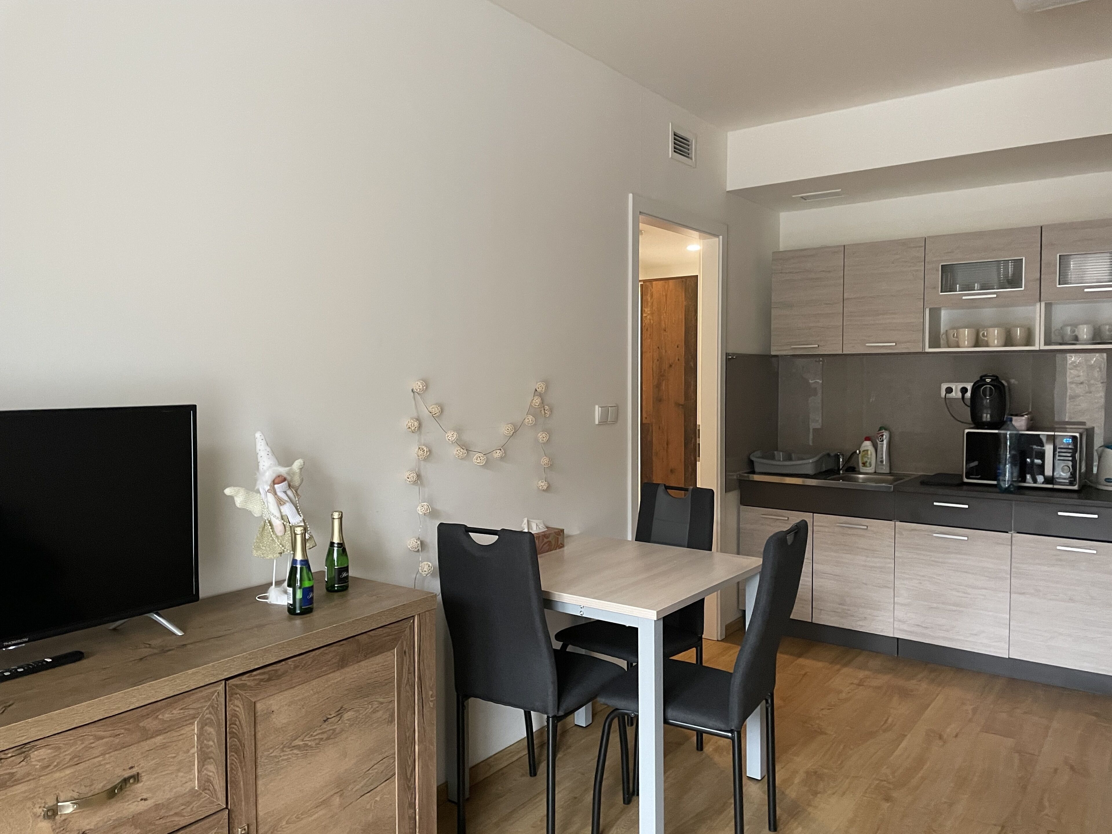A modern kitchen with wooden cabinets, a dining table with chairs, a television, and a decorative string of flowers.