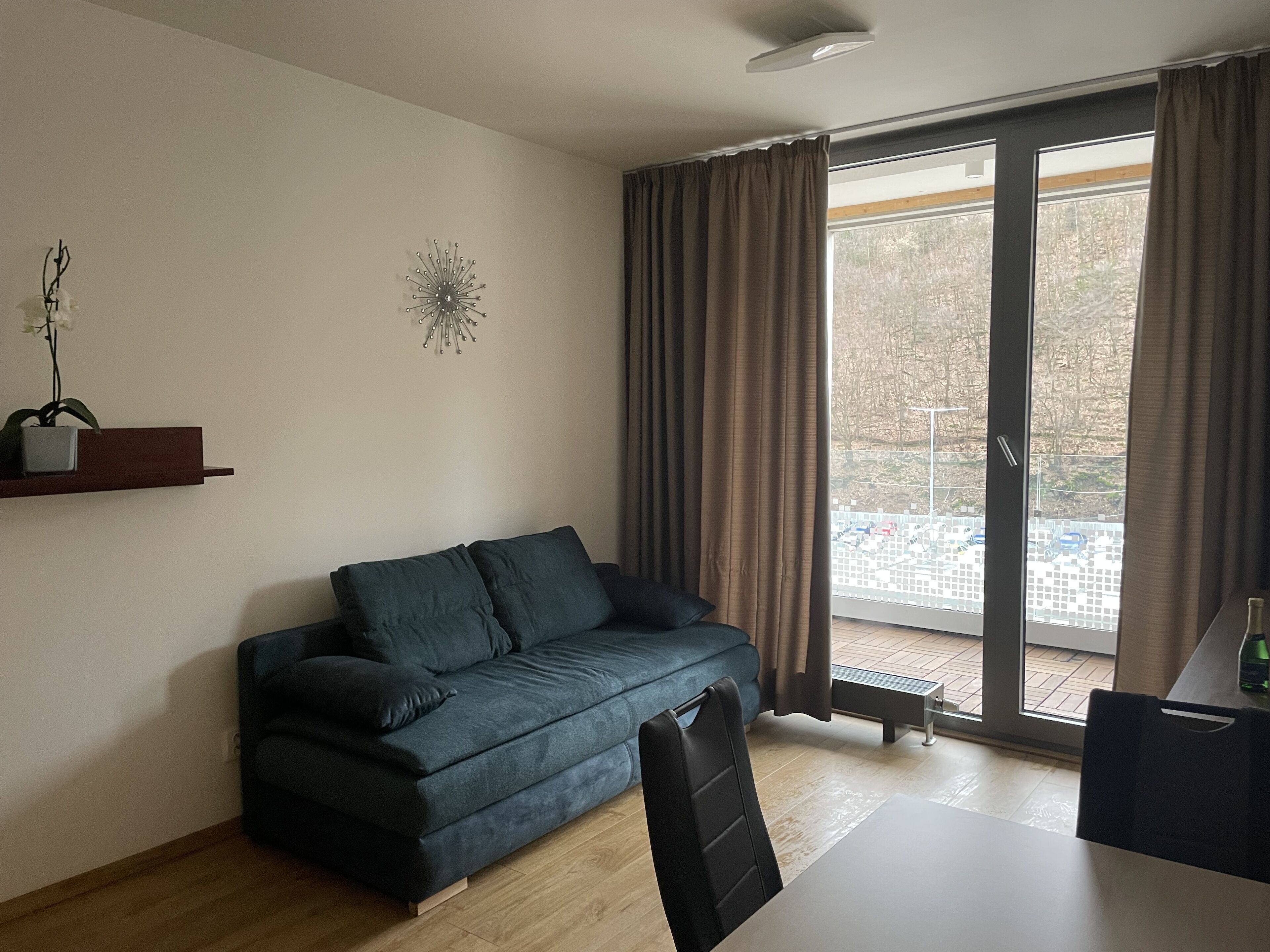 A modern living room with a dark blue sofa, a small table, and a large sliding glass door leading to an outdoor area.