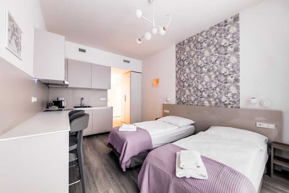 Ein modernes Hotelzimmer mit zwei Betten, einer Küchenzeile, einem Schreibtisch und einer Duschkabine.