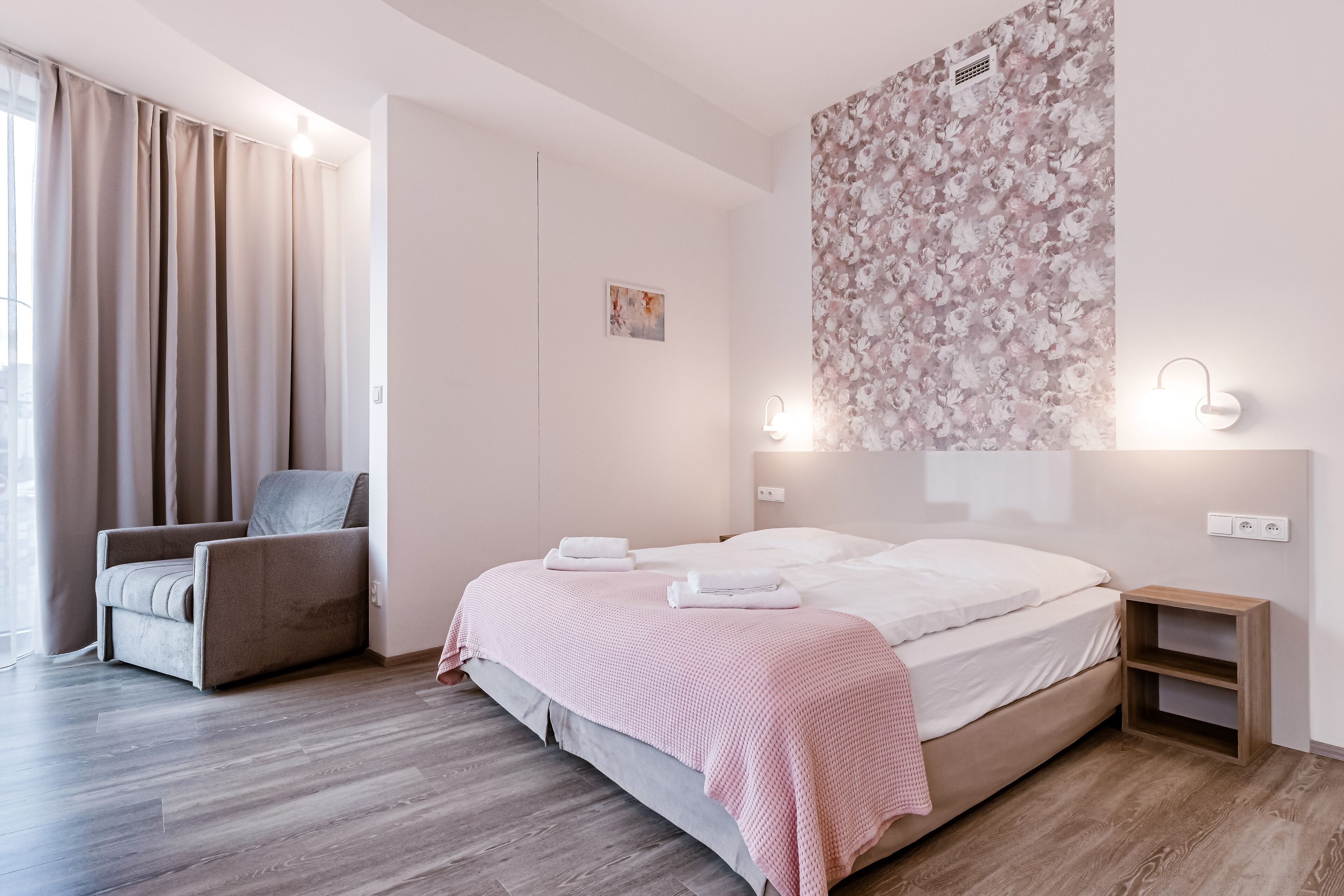 Un dormitorio moderno con una cama, una silla, una mesita de noche y un aplique de pared.