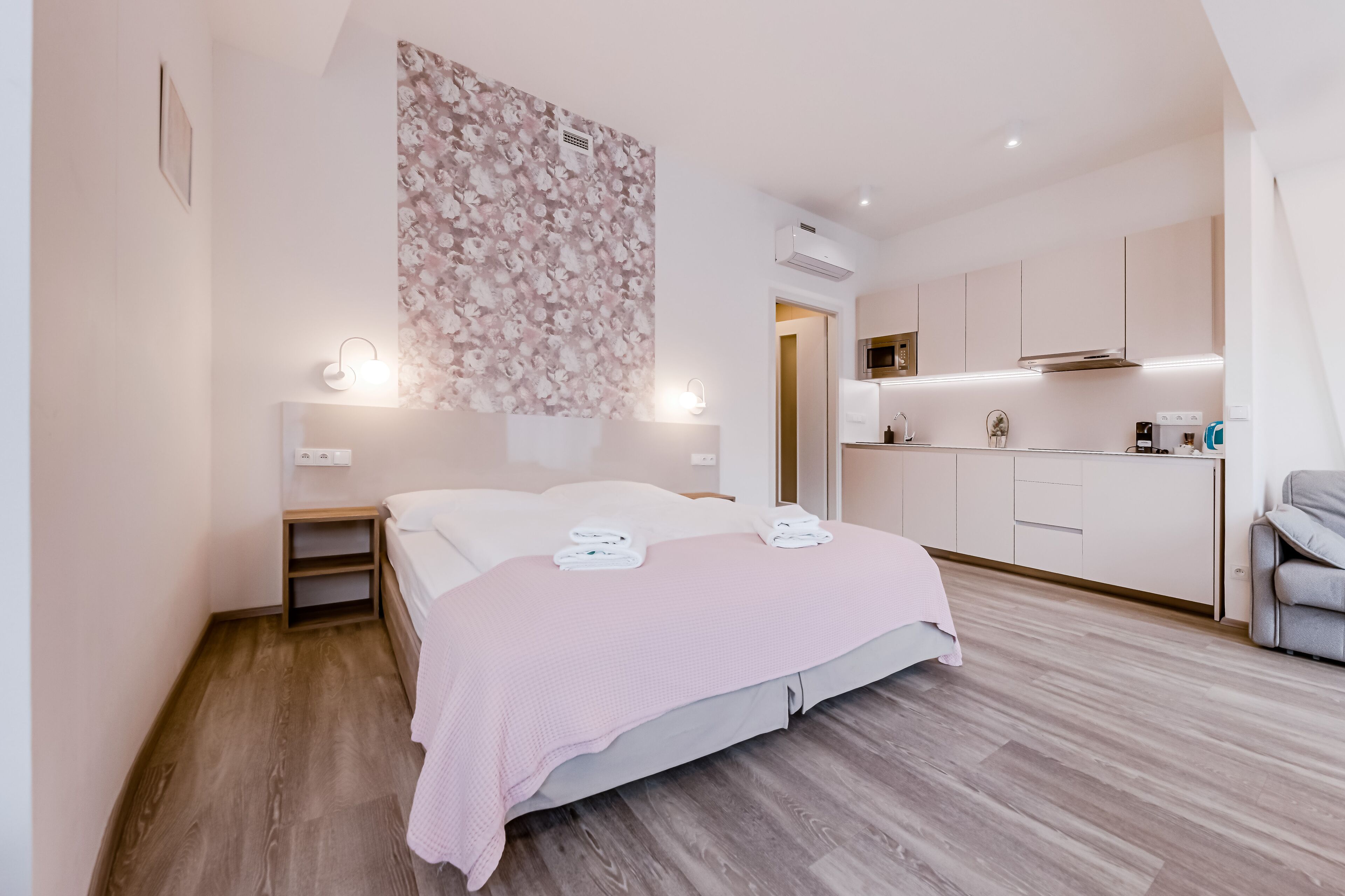 Un dormitorio moderno con suelo de madera, una cama con manta rosa, una mesita de noche y una lámpara fijada a la pared.