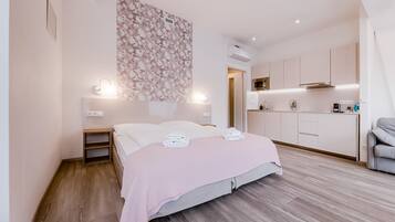 Un dormitorio moderno con suelo de madera, una cama con manta rosa, una mesita de noche y una lámpara fijada a la pared.