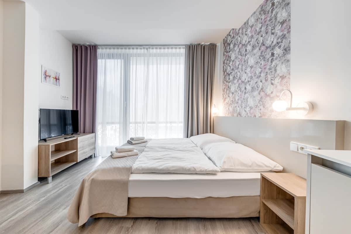 Ein modernes Hotelzimmer mit Bett, Fernseher, Schreibtisch und einem großen Fenster mit Vorhängen.
