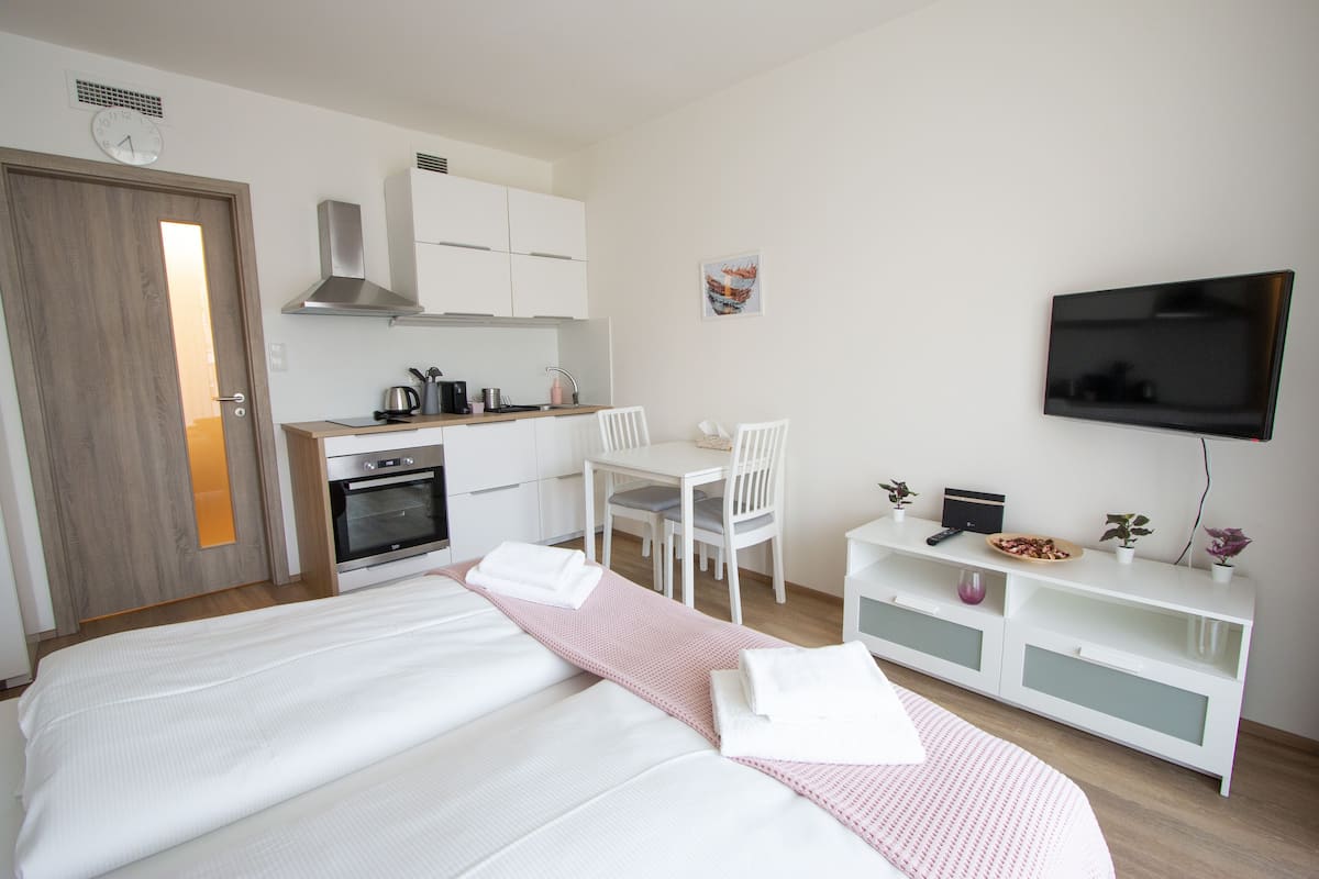 Ein Hotelzimmer mit Bett, Schreibtisch, Stuhl, Fernseher, einer Küchenzeile und einer Uhr.