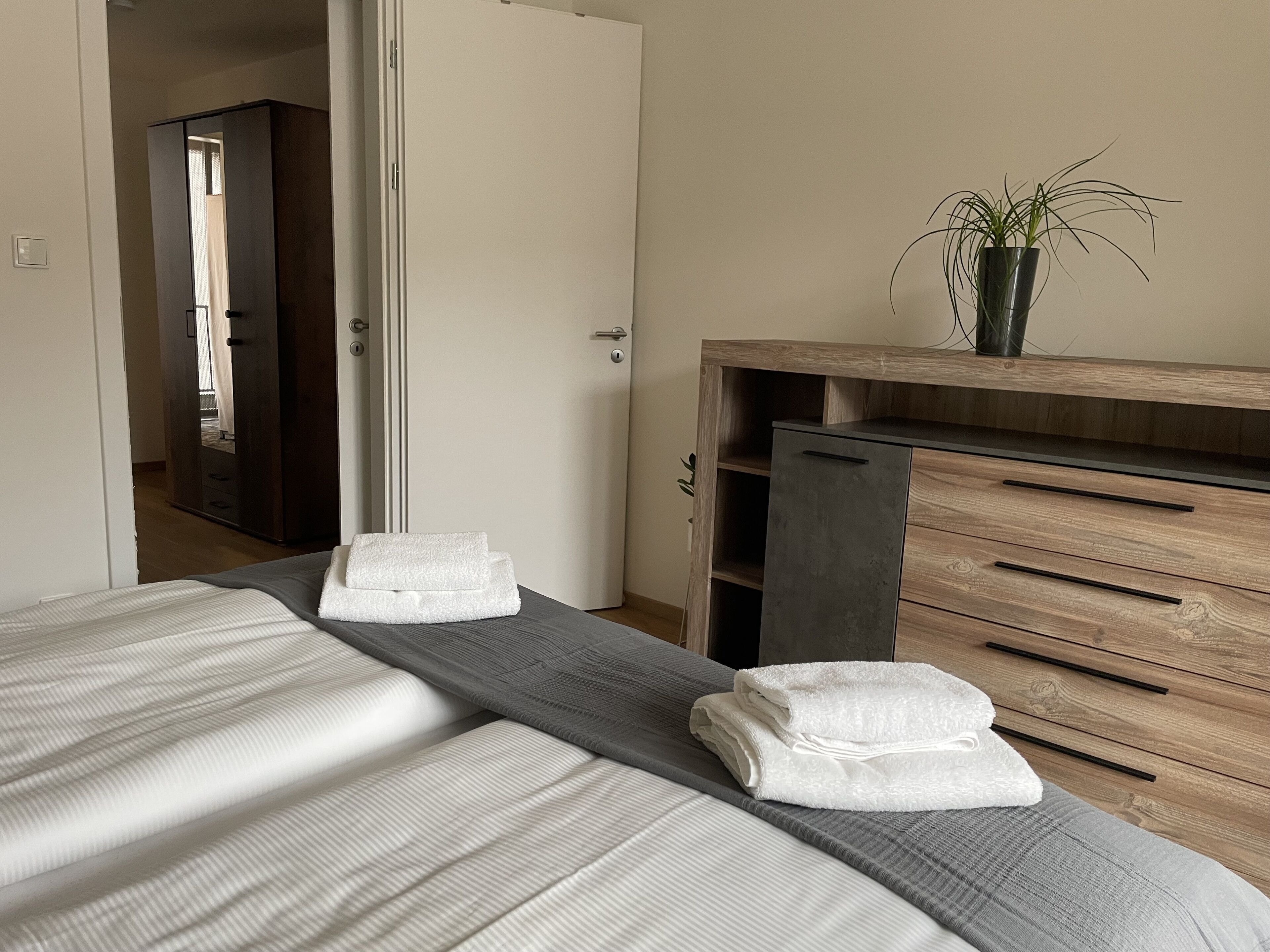 A bedroom with a bed, a wooden dresser, a mirror, and a potted plant.