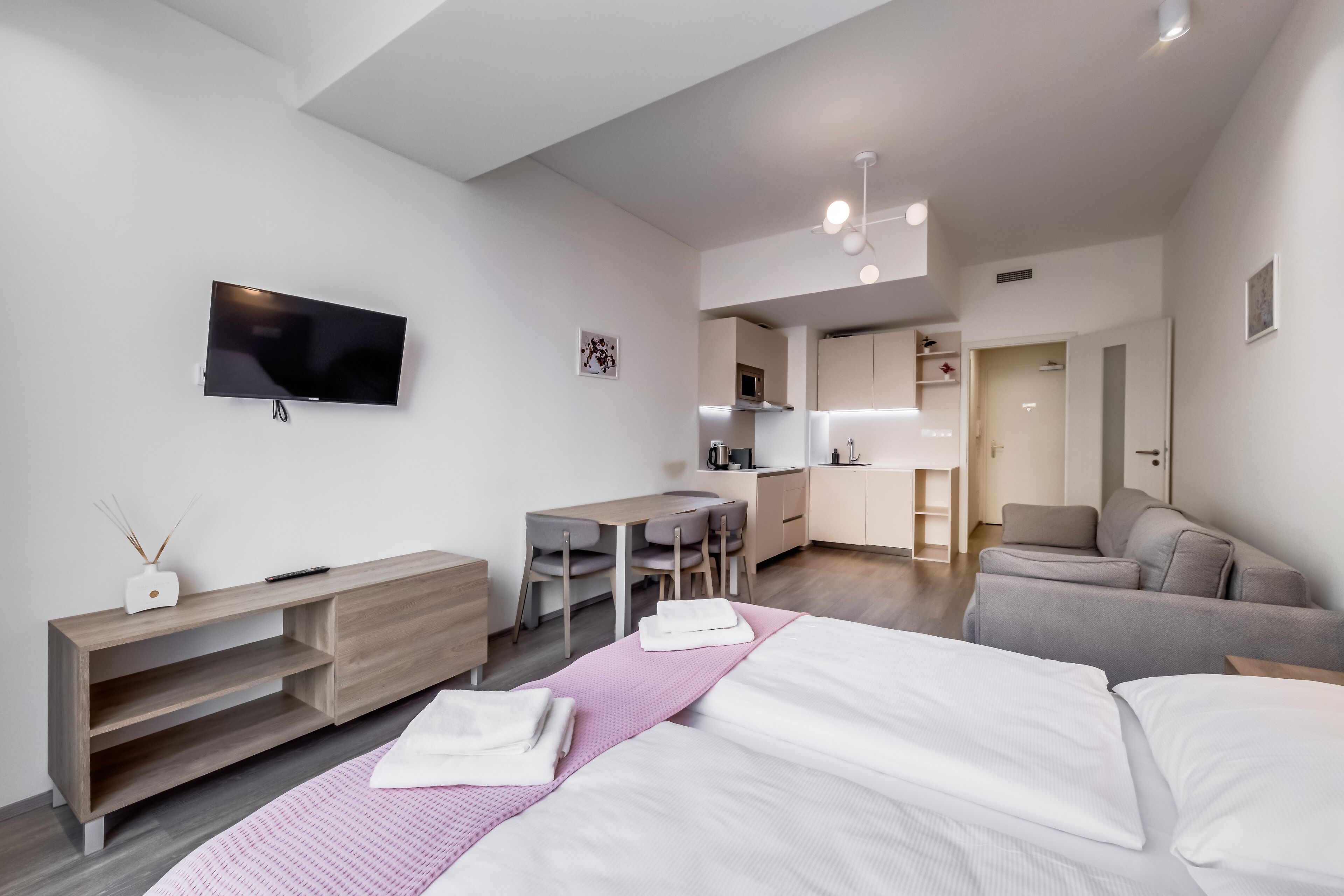 A modern hotel room with a bed, a desk, a kitchenette, and a seating area.