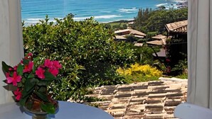 A coastal view from a balcony with a table and flowers, overlooking the sea and a village. - Pousada Vigia das Marés - Praia do Rosa - SC (Imbituba)