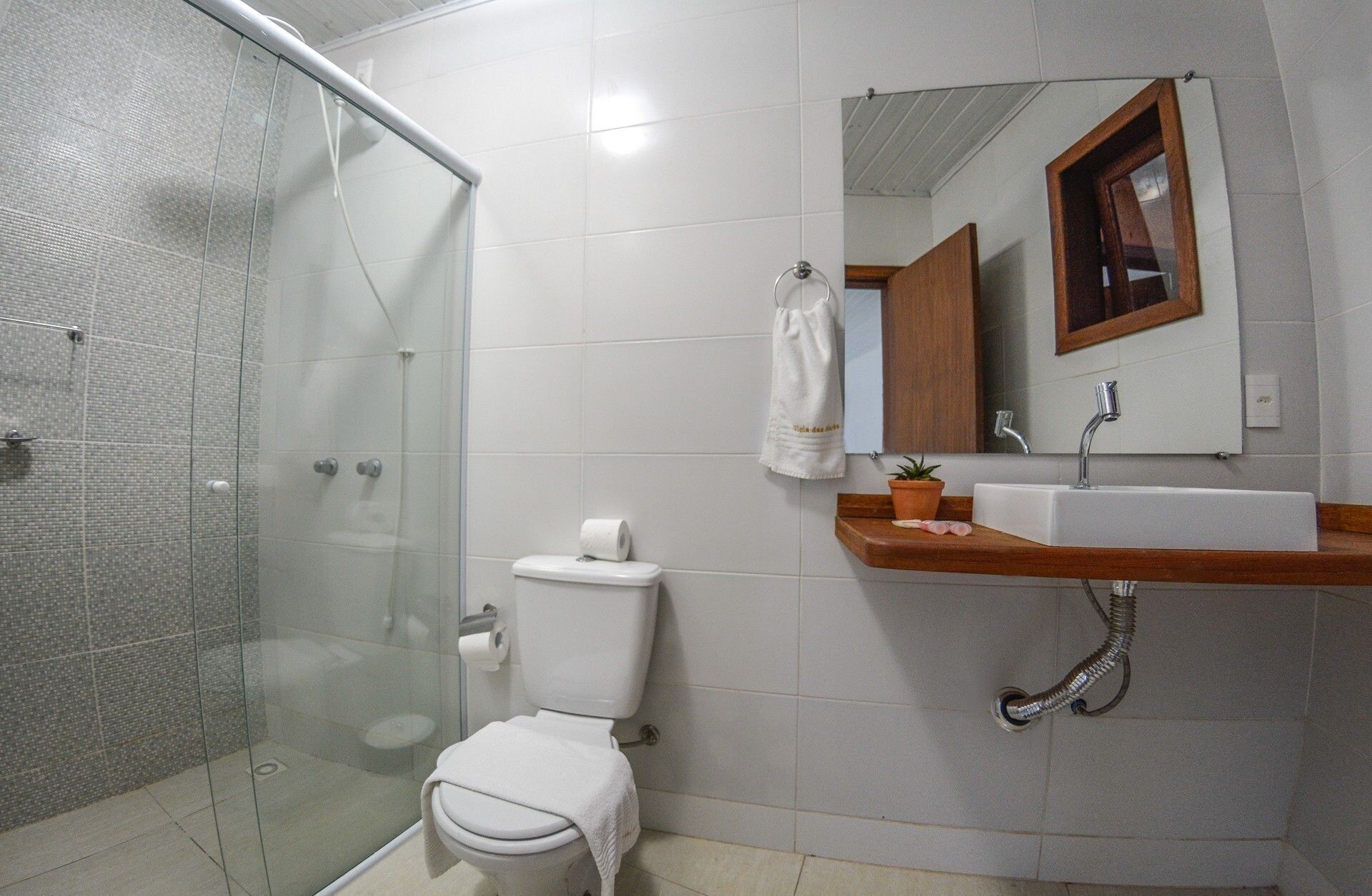 Un baño con cabina de ducha de vidrio, inodoro, lavabo con encimera de madera y espejo con marco de madera.