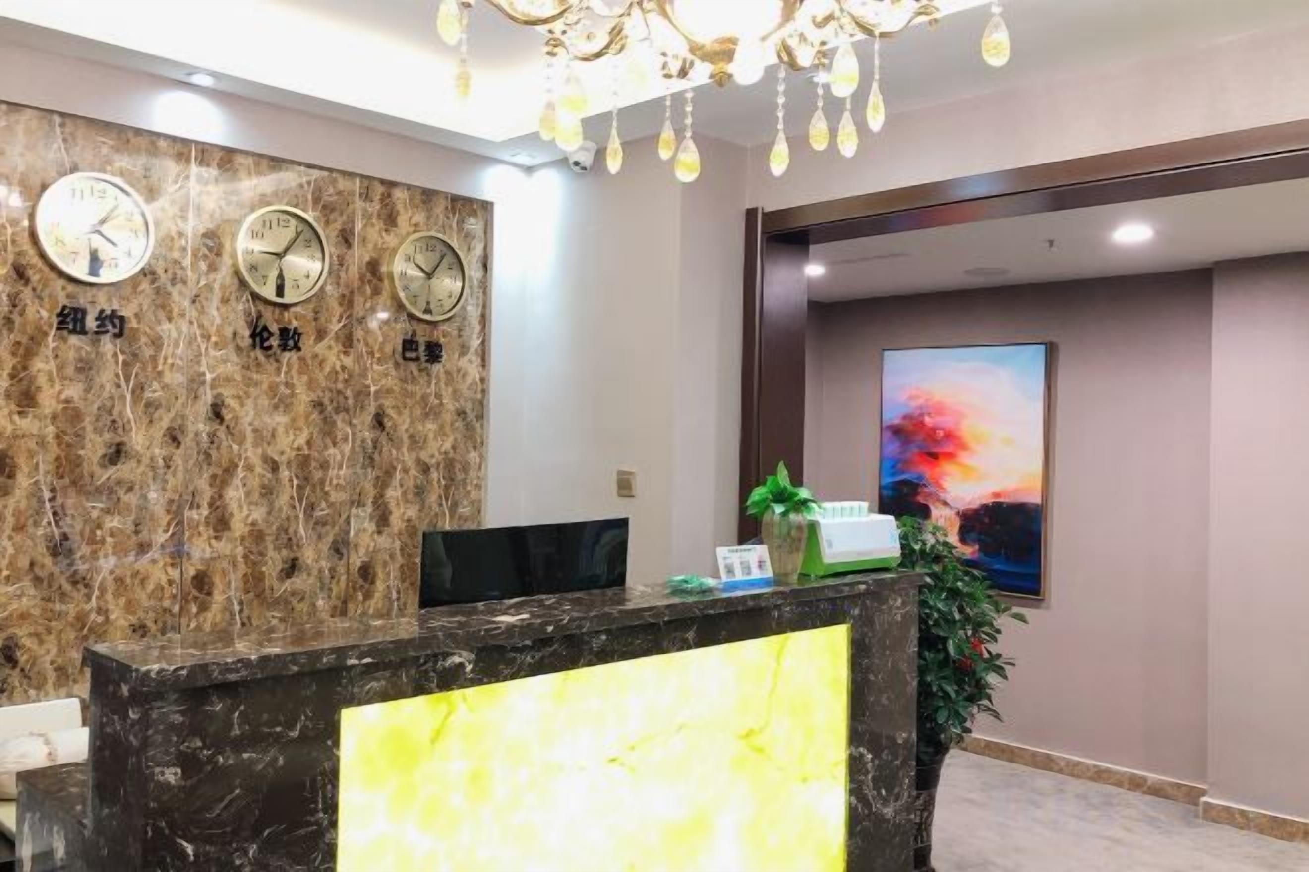 A reception desk with a marble wall, clocks, and a painting.