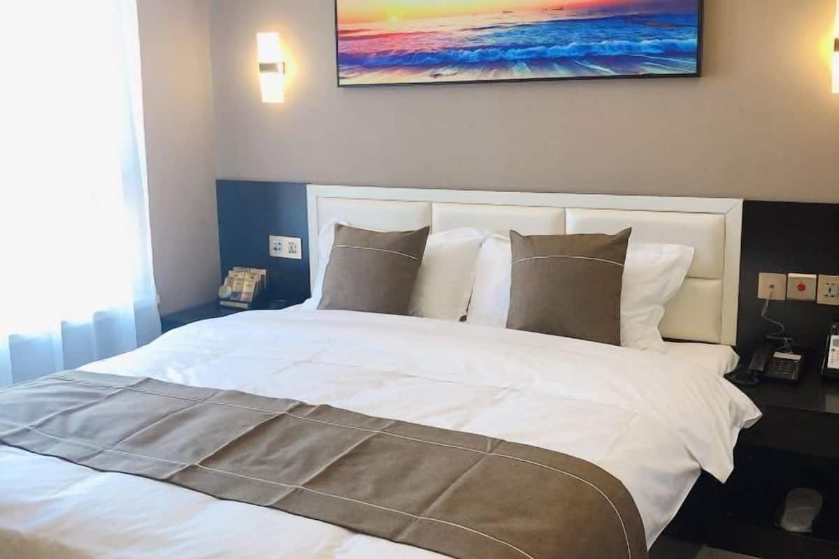 A hotel room with a large bed, a headboard, a nightstand with a phone, and a wall-mounted painting.