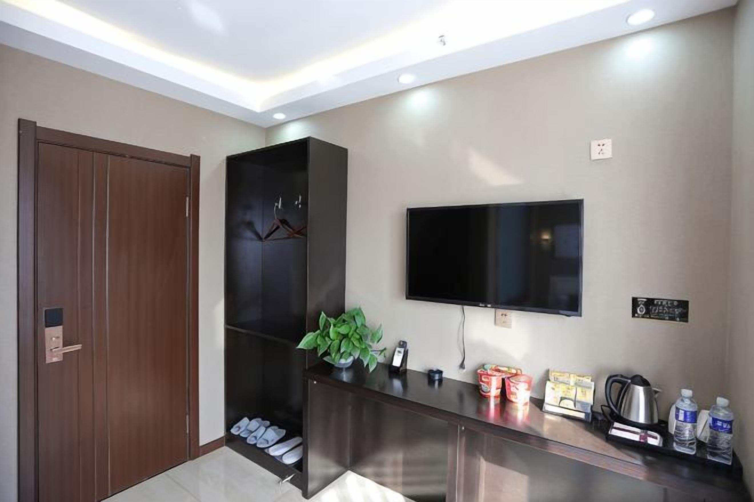 A hotel reception area with a wooden door, a black shelving unit, a flat-screen TV, and a counter with amenities.