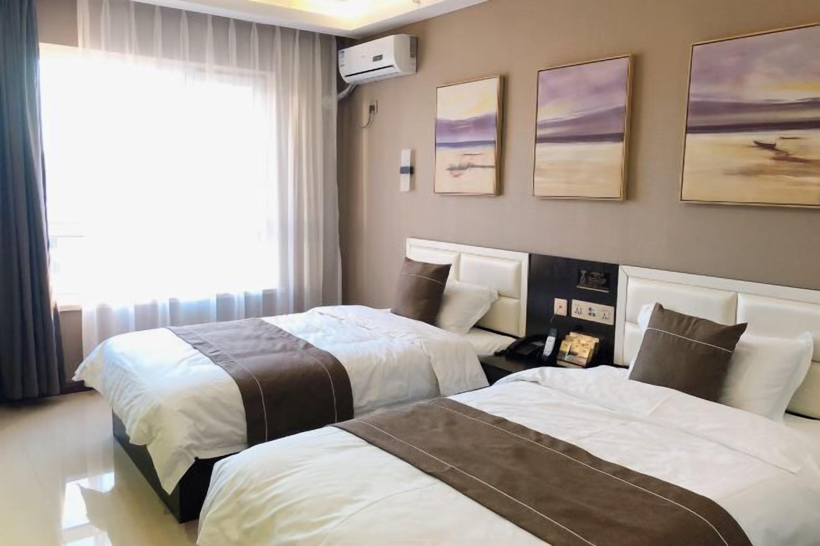 A hotel room with two beds, a large window with curtains, an air conditioning unit, and three paintings on the wall.
