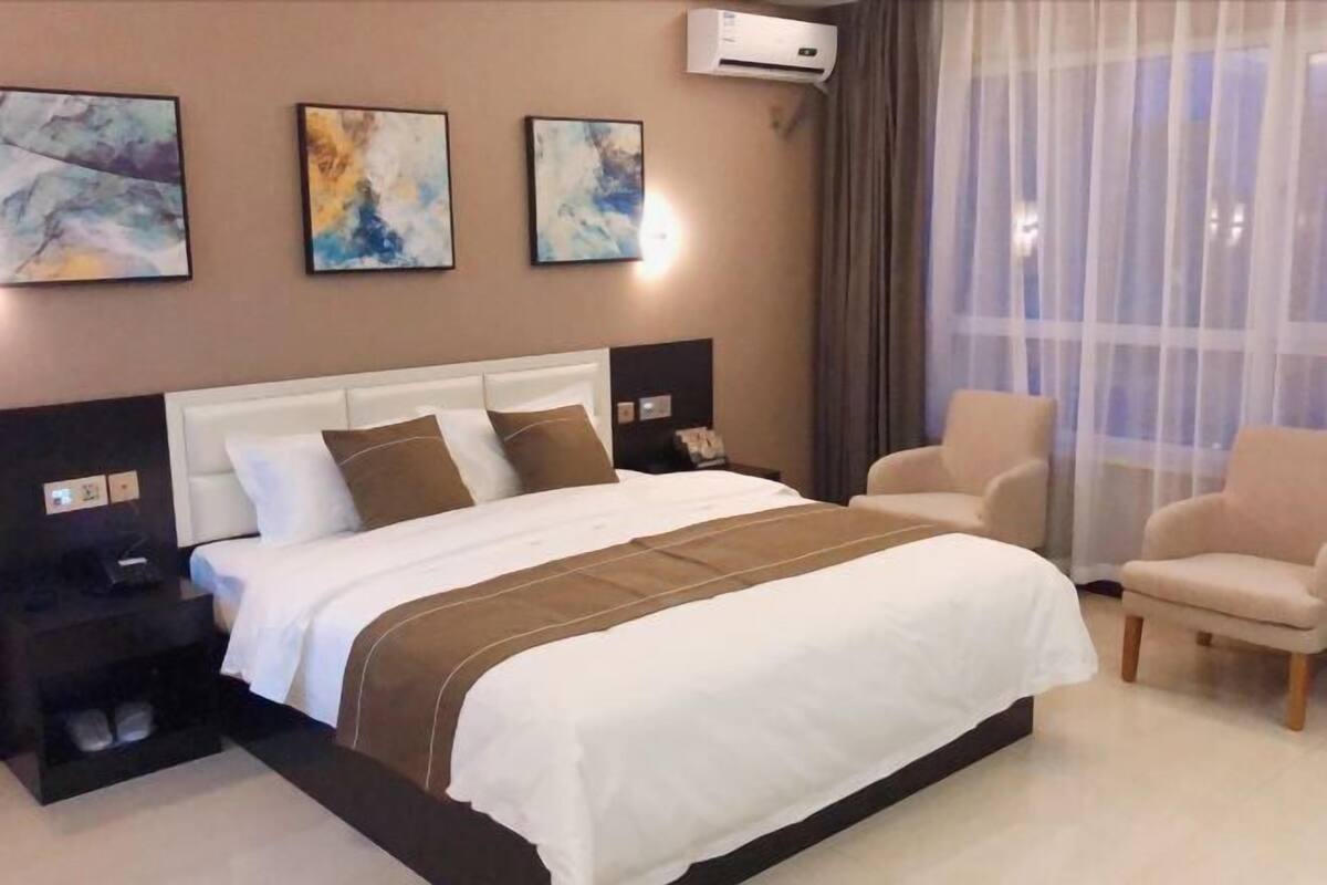 A hotel room with a large bed, two bedside tables, a chair, and three abstract paintings on the wall.