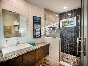 A modern bathroom with a large sink, a glass shower enclosure, and a view of the outdoors.