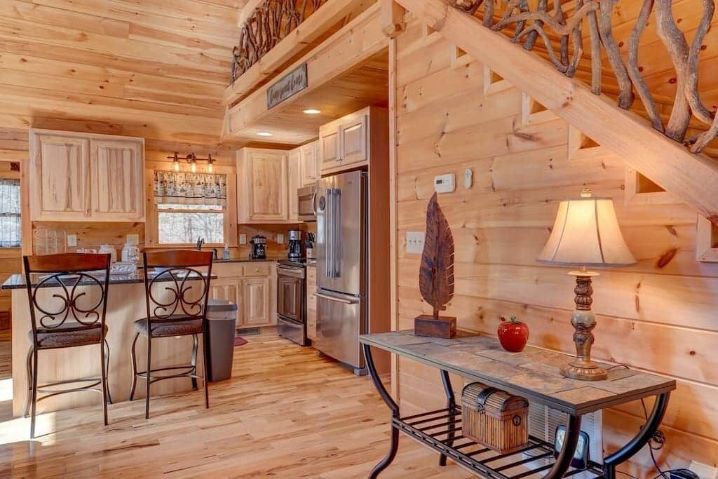 A wooden interior with a kitchen area, a dining table with chairs, and a staircase.