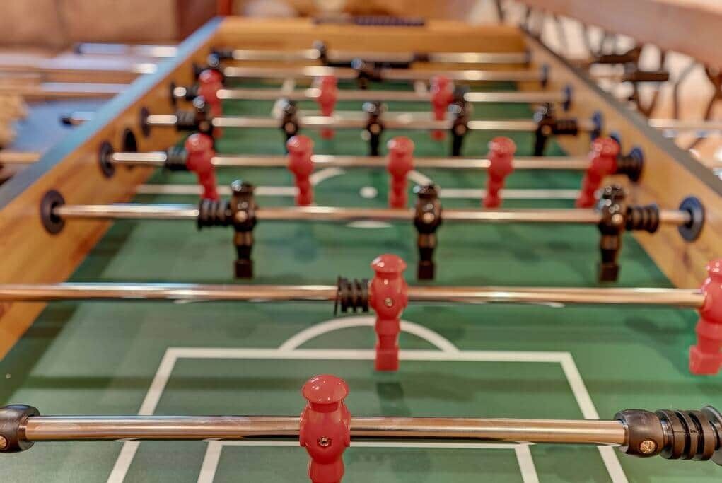 Une table de baby-foot avec un tapis de jeu vert et des figurines de joueurs rouges et noires.