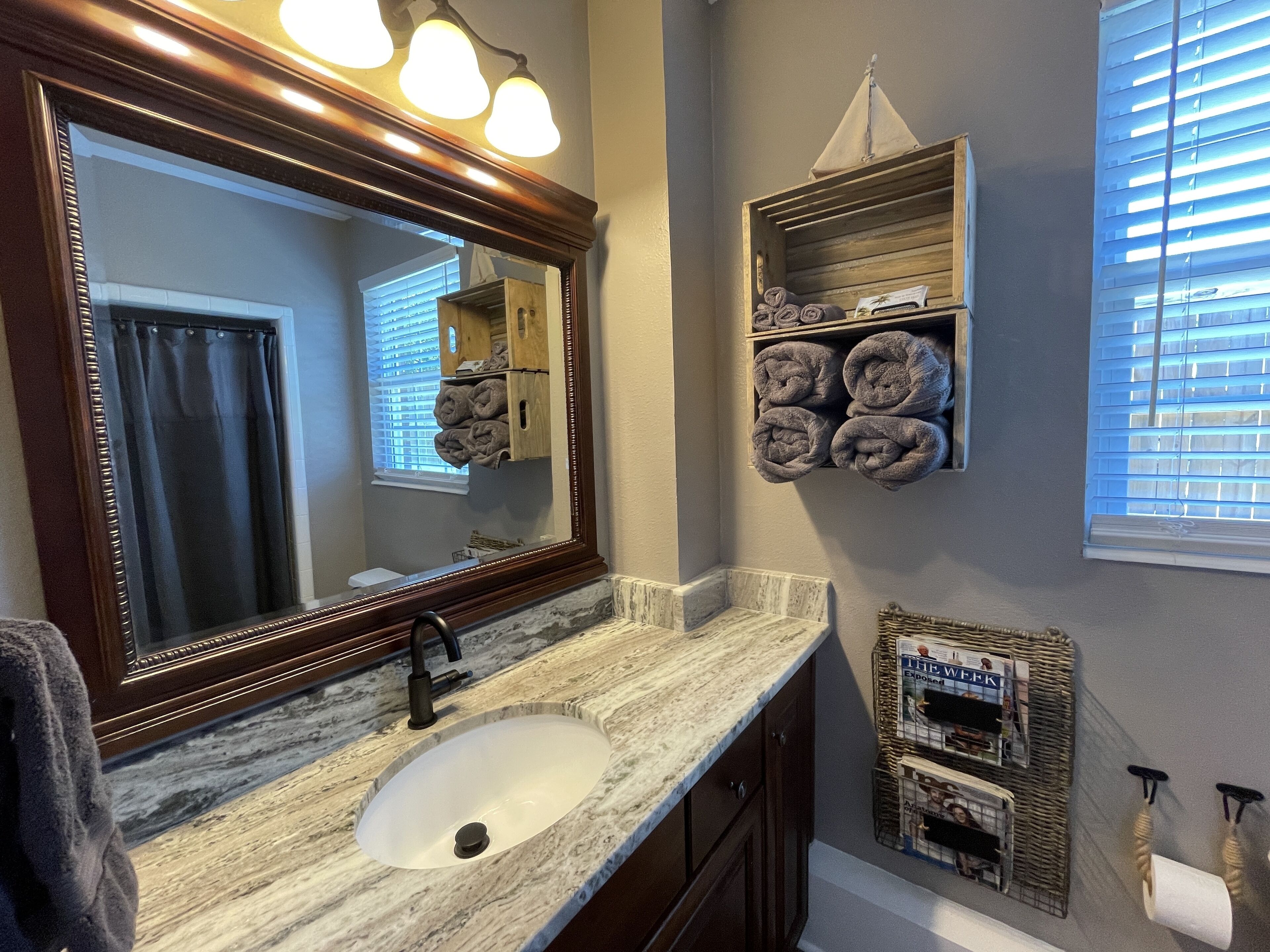 A bathroom with a marble sink, a large mirror, and towels on shelves.