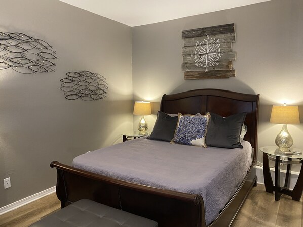 A neatly arranged bedroom with a bed, bedside tables, and decorative wall art. - Beautiful Renovated Studio Close to Pensacola Beach (Gulf Breeze)