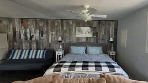 A bedroom with a bed, a chair, a ceiling fan, and a window.