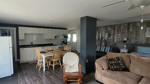 A compact kitchen with white cabinets, a dining area with wooden chairs, and a beige sofa in a living room.