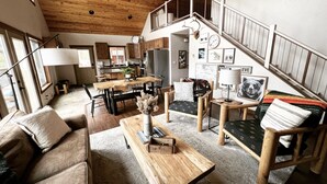 A spacious living area with a wooden ceiling, a dining table, a sofa, and a staircase leading to an upper level. - Cleveland Cabin with Mountain Views & Lake Access (Rexford)