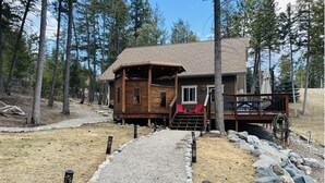 A cabin with a gravel path leading to a wooden deck, surrounded by trees. - Cleveland Cabin with Mountain Views & Lake Access (Rexford)