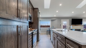 Una cocina moderna con armarios de madera oscura, una isla grande con encimera blanca, electrodomésticos de acero inoxidable y vistas al exterior.