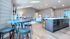 Cocina moderna con una isla central, taburetes de bar y una zona de comedor con sofá y mesa.