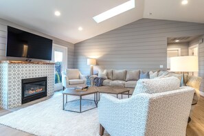 A modern living room with a fireplace, a large TV, and a cozy seating area with patterned chairs and a sofa.