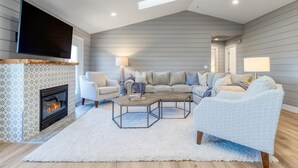 Una sala de estar moderna con chimenea, un televisor grande montado en la pared y un rincón de estar acogedor con sofá y sillones.