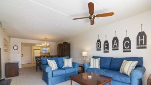 A living room with two blue sofas, a wooden coffee table, a ceiling fan, and wall decorations spelling out "BEACH". - Excellent Beach Location ~ Pool ~ Great Price! (Saint Augustine)