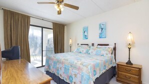 A hotel room with a bed, a desk, a chair, a ceiling fan, two wall-mounted lamps, and a window with curtains. - Excellent Beach Location ~ Pool ~ Great Price! (Saint Augustine)