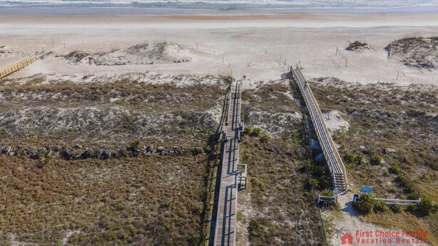 A beach with a long wooden boardwalk leading to the shore, surrounded by sparse vegetation. - Excellent Beach Location ~ Pool ~ Great Price! (Saint Augustine)