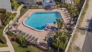 An aerial view of a swimming pool surrounded by palm trees and lounge chairs, with a parking area and a building in the background. - Excellent Beach Location ~ Pool ~ Great Price! (Saint Augustine)