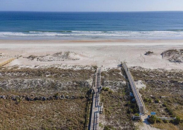 A beach with a long wooden boardwalk leading to the shore, surrounded by sparse vegetation. - Excellent Beach Location ~ Pool ~ Great Price! (Saint Augustine)