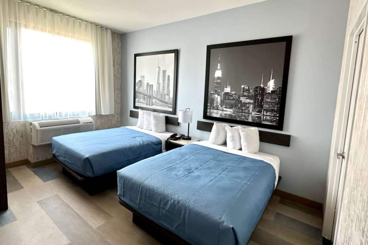 A hotel room with two beds, a cityscape view, and a window with curtains.