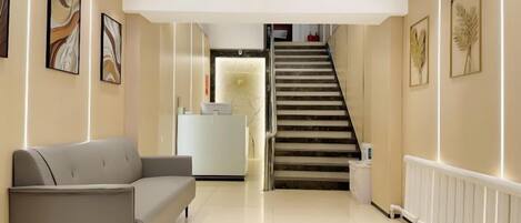 Un vestíbulo de hotel con una recepción, una escalera y un sofá.