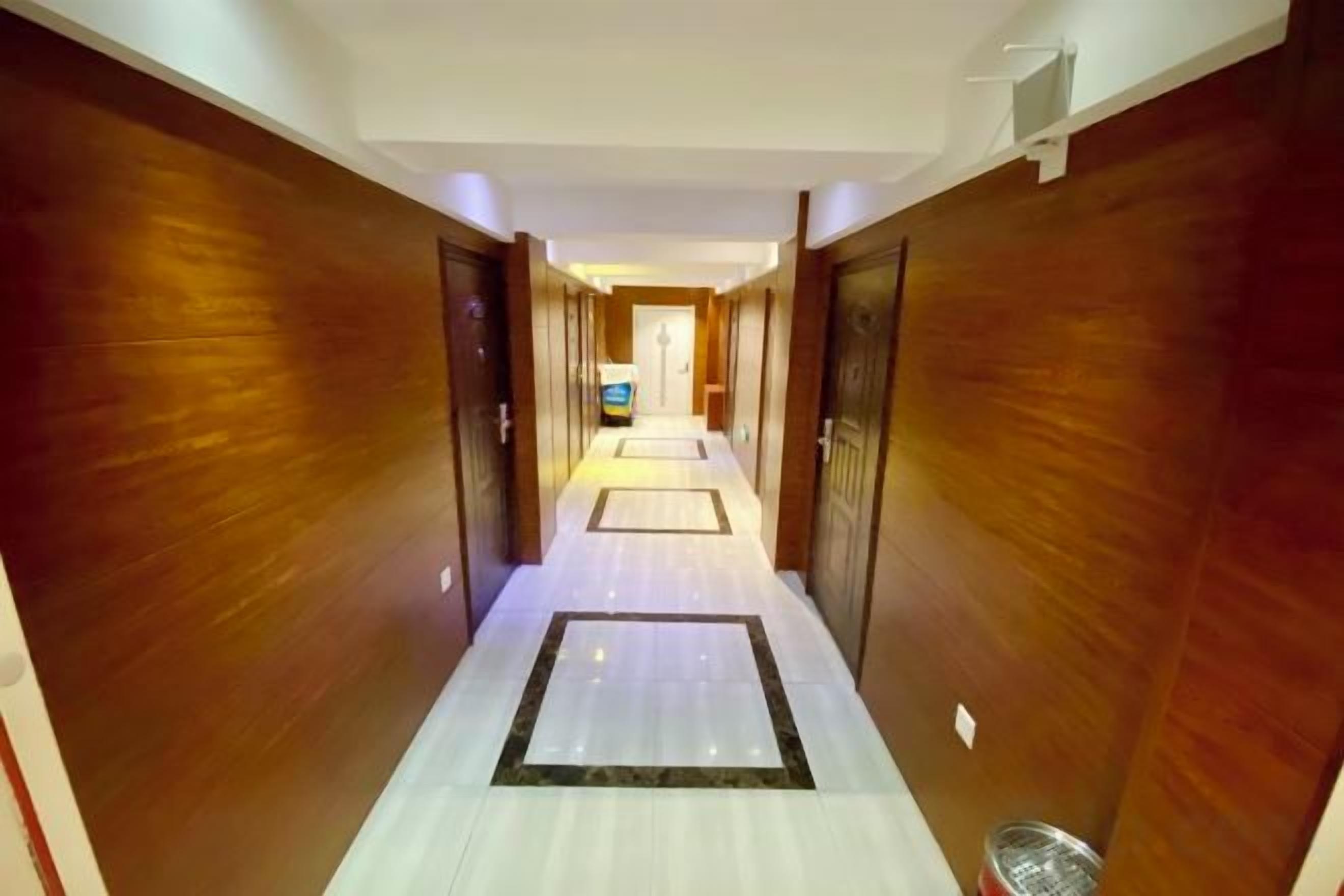 A hotel corridor with wooden walls and a tiled floor, leading to a room with a television.