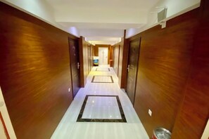 A hotel corridor with wooden walls and a tiled floor, leading to a room with a television. - Jinyi Business Hotel (Changchun)
