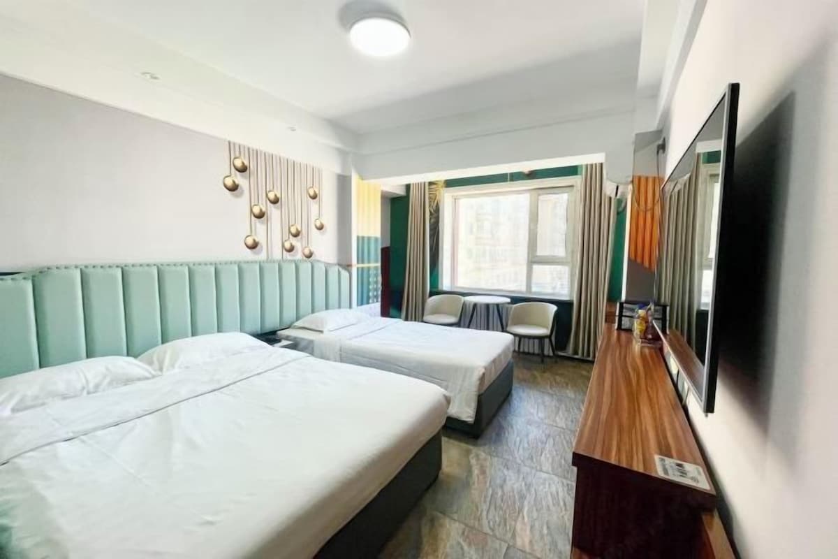 A hotel room with two beds, a small table, a TV, and a window with curtains.