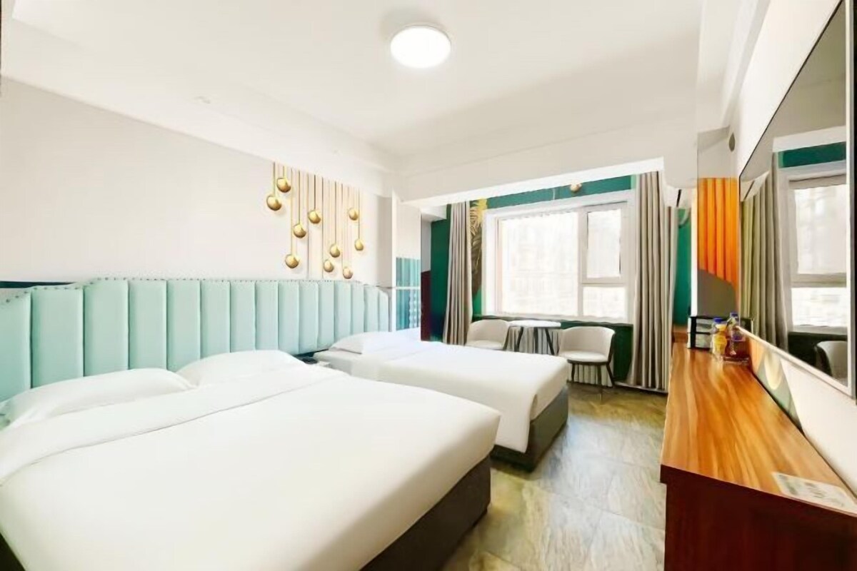 A hotel room with two beds, a wooden desk, a small table, and a window with curtains.