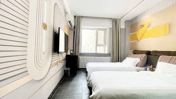 A hotel room with two beds, a large window, a radiator, and a wall-mounted TV.