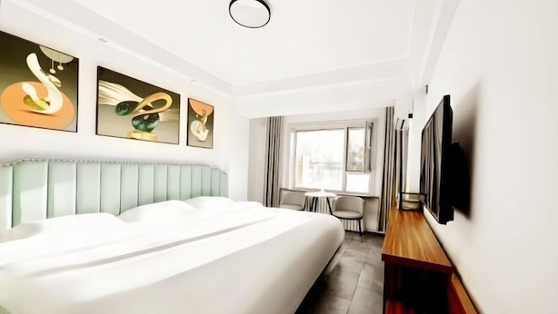 A modern hotel room with a large bed, a TV mounted on the wall, and artwork above the bed. - Jinyi Business Hotel (Changchun)