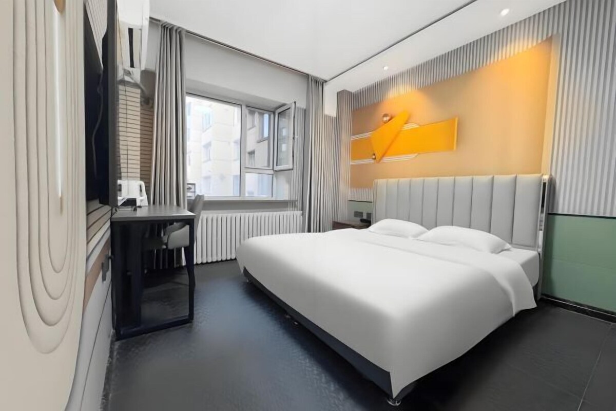 A modern hotel room with a large bed, a desk, and a window.