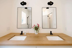 Ein Badezimmer mit zwei Waschbecken, einem Spiegel und einer Blumenvase.