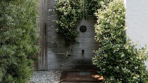 Un jardín con cerramiento de madera, un pequeño estanque y un edificio blanco al fondo.