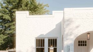 Una casa moderna con fachada blanca, un ventanal grande y un pequeño patio con plantas.
