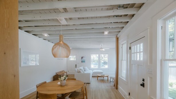 Un interior moderno con una mesa de comedor de madera, sofás blancos y un ventanal grande.