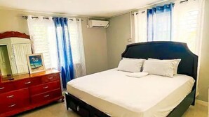 A bedroom with a bed, a dresser, and a mirror. - Gated 2BR Apartment + Enjoy A/C & Wi-Fi + From 100/Night (Kingston 10)