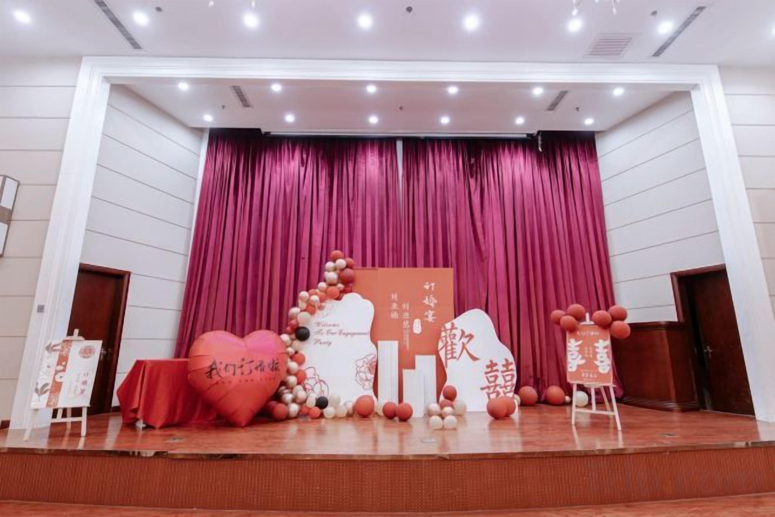 A stage with a red curtain backdrop, a heart-shaped decoration, and a sign with text.